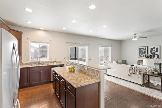 kitchen with light stone countertops, sink, dark hardwood / wood-style flooring, white fridge, and a kitchen island