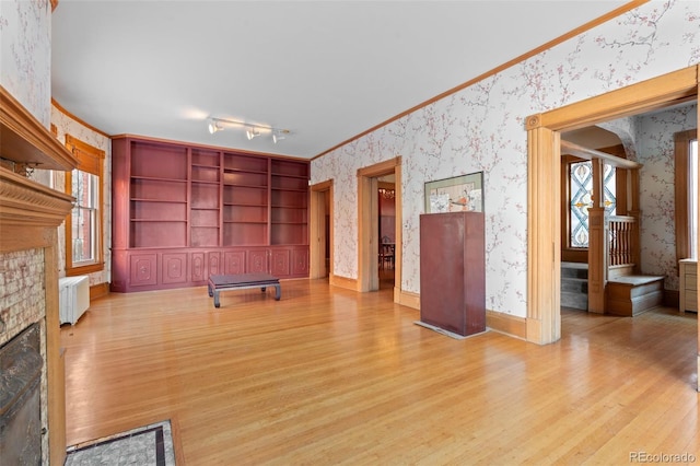 unfurnished living room featuring ornamental molding, a brick fireplace, and light wood-type flooring