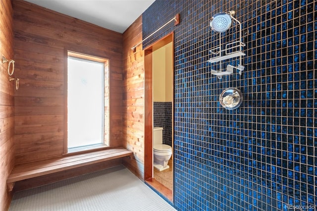 bathroom featuring toilet, tile patterned flooring, tile walls, and a tile shower