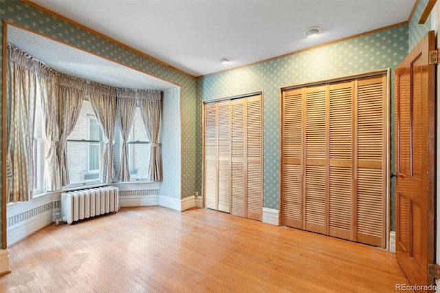 unfurnished bedroom featuring multiple closets, ornamental molding, radiator heating unit, and hardwood / wood-style flooring