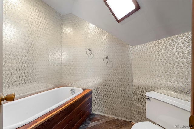 bathroom featuring lofted ceiling, toilet, wood-type flooring, tile walls, and a tub