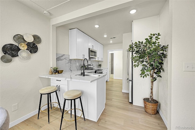 kitchen featuring white cabinetry, a kitchen bar, appliances with stainless steel finishes, backsplash, and sink