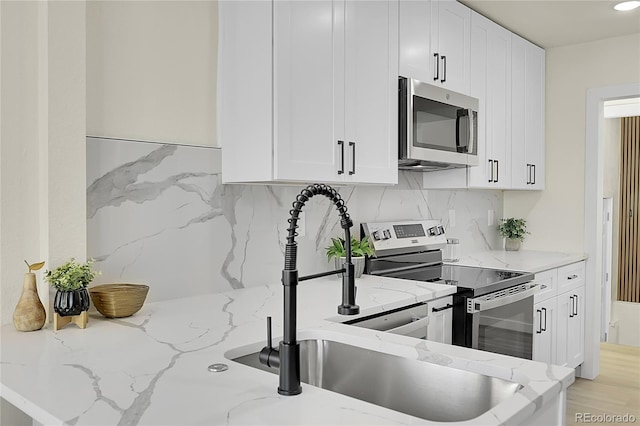 kitchen featuring stainless steel appliances, backsplash, white cabinetry, and light stone counters