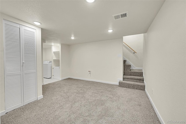 basement with a textured ceiling, light carpet, and washer / clothes dryer