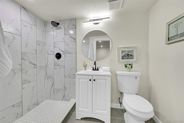 bathroom featuring a textured ceiling, toilet, tiled shower, and vanity