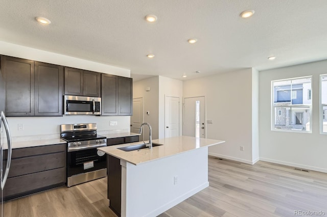 kitchen with appliances with stainless steel finishes, dark brown cabinets, a sink, and light wood-type flooring