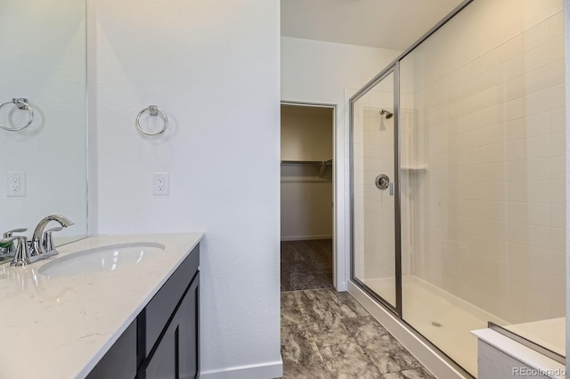 bathroom with baseboards, vanity, a walk in closet, and a stall shower