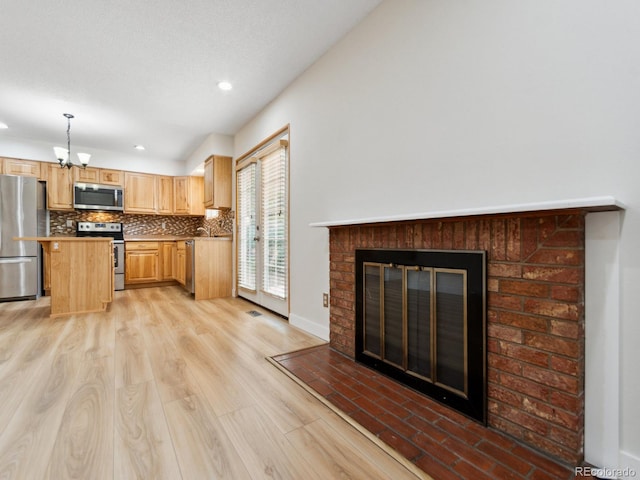 kitchen featuring light wood-type flooring, pendant lighting, brick wall, a fireplace, and stainless steel appliances