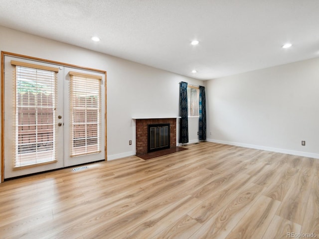 unfurnished living room featuring light wood-type flooring, a brick fireplace, and french doors