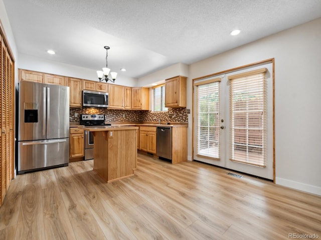 kitchen featuring appliances with stainless steel finishes, light hardwood / wood-style flooring, decorative backsplash, a kitchen island, and hanging light fixtures