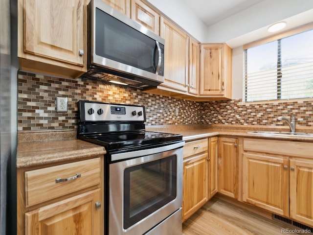 kitchen with backsplash, sink, light hardwood / wood-style flooring, light brown cabinetry, and stainless steel appliances