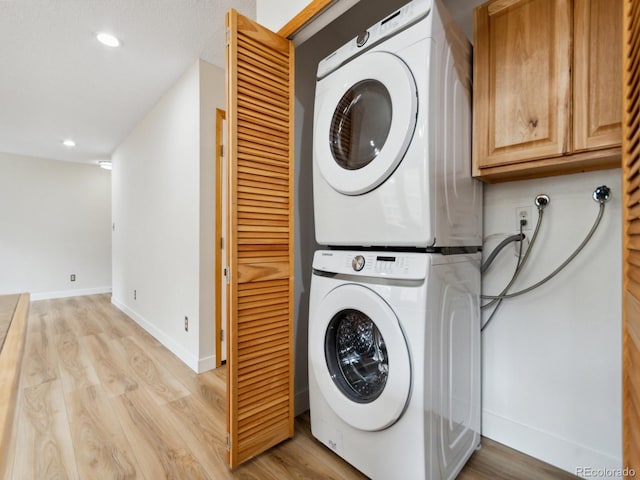 laundry area with stacked washer / drying machine and light hardwood / wood-style flooring