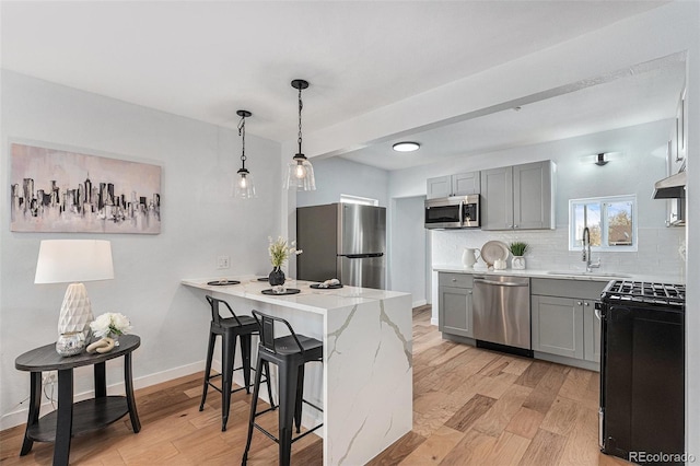 kitchen with stainless steel appliances, gray cabinets, a sink, a peninsula, and light wood-style flooring