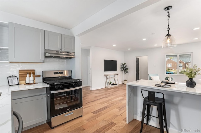 kitchen featuring gas range, under cabinet range hood, gray cabinets, tasteful backsplash, and light stone counters