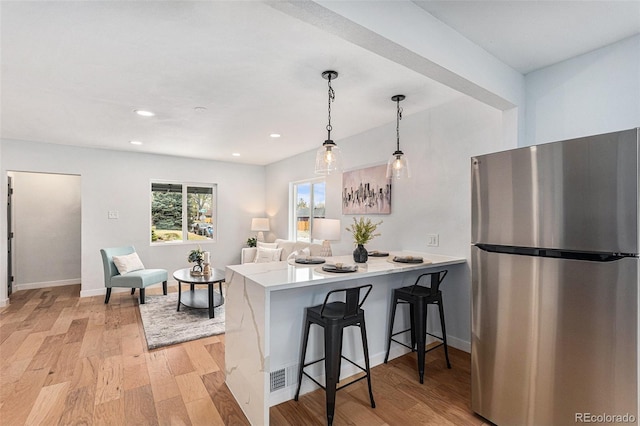 kitchen with freestanding refrigerator, light wood-style floors, a kitchen bar, a peninsula, and recessed lighting
