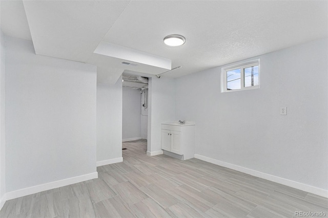 basement with light wood-style floors, baseboards, and a sink