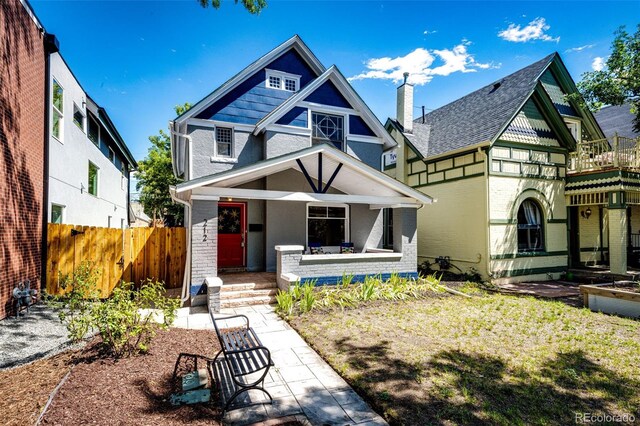 view of front of house featuring covered porch, brick siding, and fence