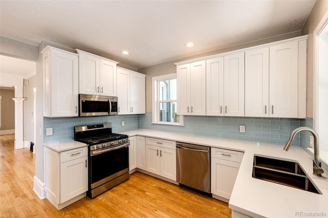 kitchen featuring light wood-type flooring, backsplash, sink, appliances with stainless steel finishes, and white cabinets