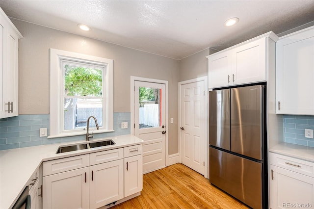 kitchen featuring light wood-type flooring, white cabinetry, backsplash, sink, and appliances with stainless steel finishes