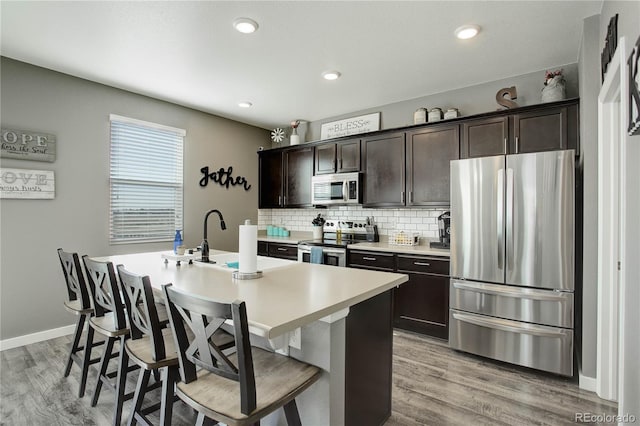 975 Alta St, Lochbuie, CO 80603 - kitchen featuring stainless steel appliances, dark brown cabinetry, light wood finished floors, decorative backsplash, and a breakfast bar area