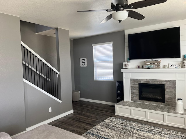 975 Alta St, Lochbuie, CO 80603 - living room featuring dark wood-type flooring, a tiled fireplace, a ceiling fan, baseboards, and a textured ceiling