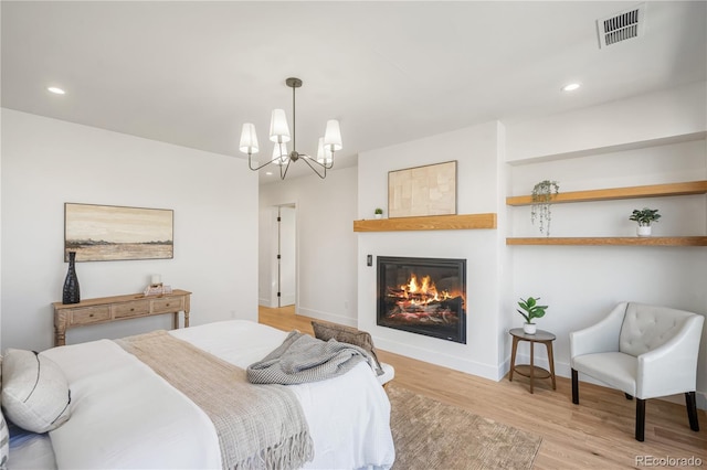 bedroom with a large fireplace, light hardwood / wood-style floors, and a chandelier