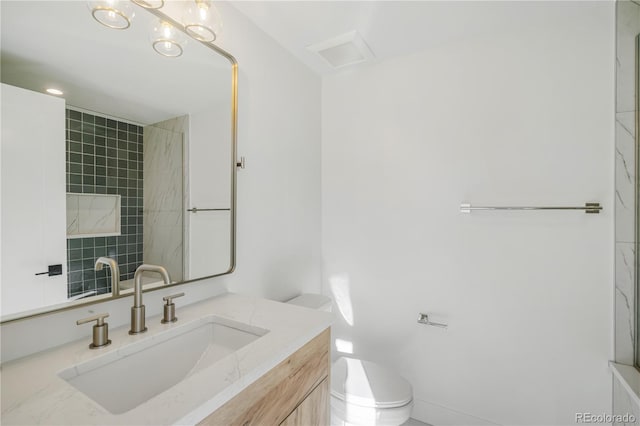 bathroom with a tile shower, vanity, and toilet