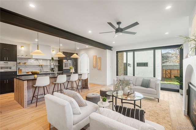 living room featuring ceiling fan, sink, and light wood-type flooring