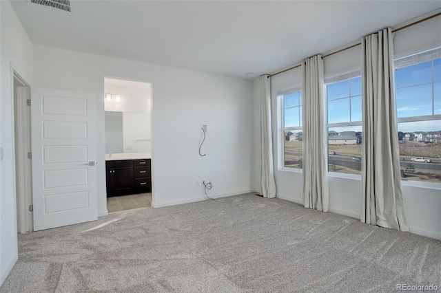 unfurnished bedroom featuring light colored carpet and ensuite bath