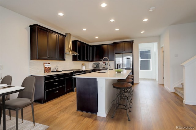 kitchen featuring sink, a kitchen breakfast bar, decorative backsplash, a kitchen island with sink, and wall chimney exhaust hood