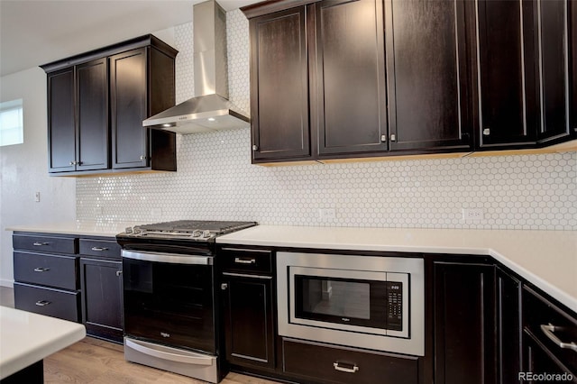 kitchen featuring tasteful backsplash, wall chimney range hood, dark brown cabinets, and stainless steel appliances