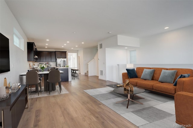 living area featuring light wood-style floors, recessed lighting, visible vents, and stairway