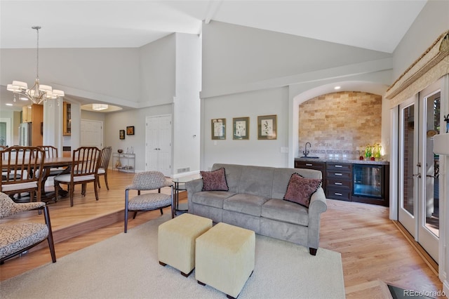 living room featuring beverage cooler, high vaulted ceiling, an inviting chandelier, and light hardwood / wood-style flooring