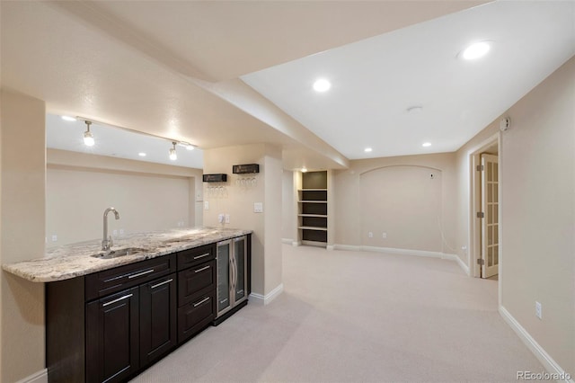 bar with dark brown cabinets, beverage cooler, track lighting, light colored carpet, and sink