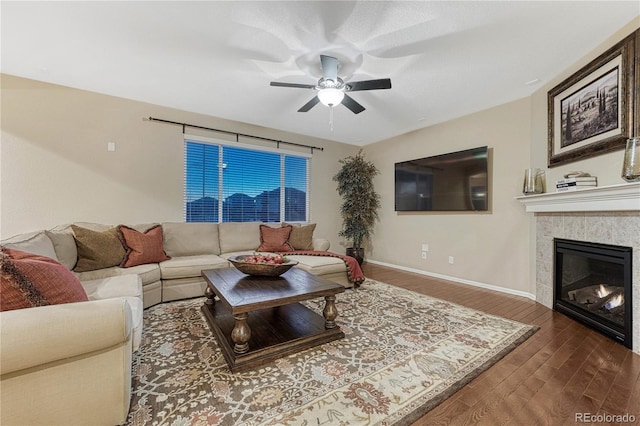 living area with a tile fireplace, ceiling fan, baseboards, and wood finished floors