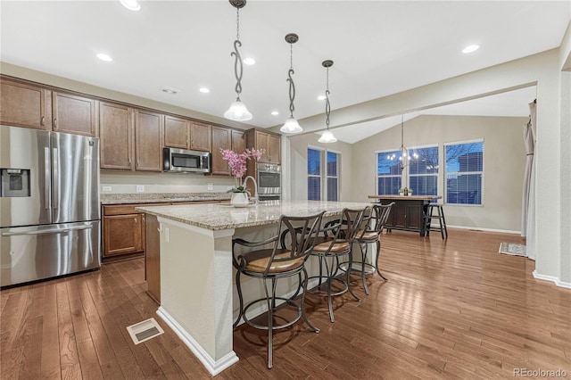 kitchen with dark wood finished floors, lofted ceiling, a kitchen breakfast bar, a center island with sink, and appliances with stainless steel finishes