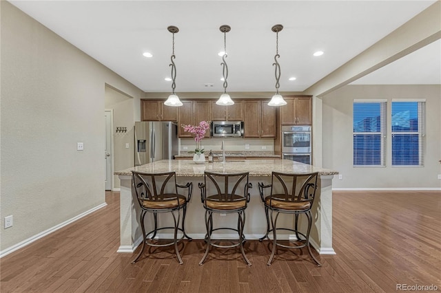 kitchen with a sink, a large island, dark wood-style flooring, light stone countertops, and appliances with stainless steel finishes