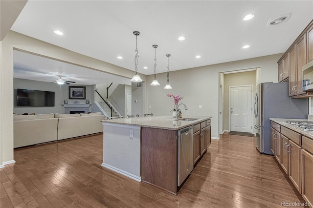 kitchen featuring a kitchen island with sink, a sink, appliances with stainless steel finishes, and dark wood-style flooring