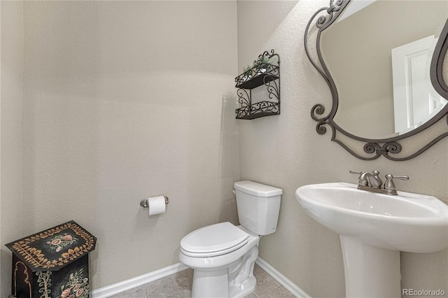 half bathroom with toilet, tile patterned flooring, a sink, and baseboards