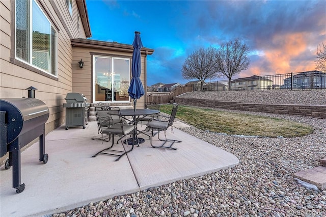 patio terrace at dusk with grilling area, outdoor dining area, and a fenced backyard