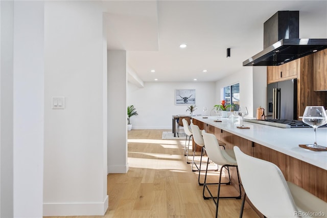 kitchen with stainless steel appliances, island exhaust hood, a breakfast bar, and light hardwood / wood-style floors