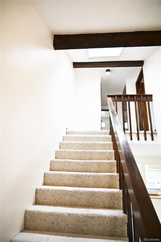 stairs featuring a skylight and beam ceiling