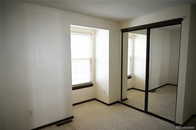 unfurnished bedroom featuring visible vents, a textured ceiling, baseboards, and multiple windows