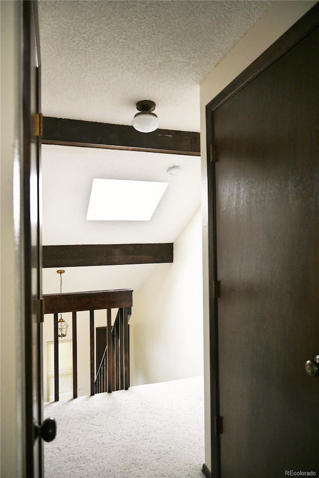 hall featuring a skylight, beamed ceiling, a textured ceiling, and an upstairs landing