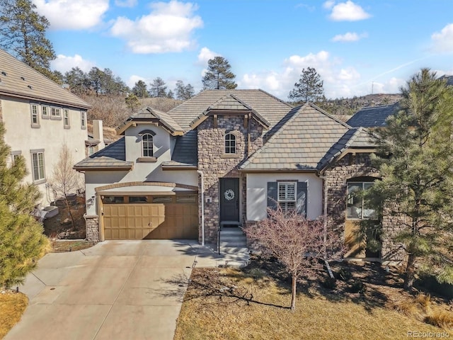 french country style house featuring driveway, stone siding, a garage, and stucco siding