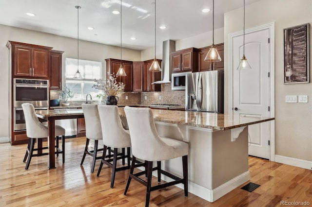 kitchen featuring tasteful backsplash, light wood finished floors, wall chimney exhaust hood, and stainless steel appliances