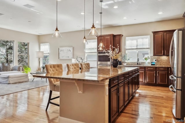 kitchen with a breakfast bar, open floor plan, appliances with stainless steel finishes, light wood-type flooring, and a center island