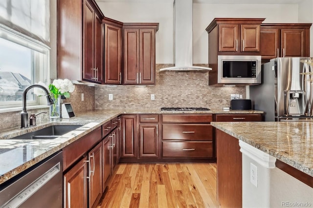 kitchen with stainless steel appliances, a sink, wall chimney exhaust hood, light wood finished floors, and tasteful backsplash