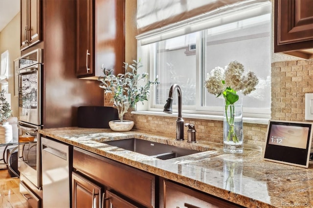 kitchen featuring light stone counters, stainless steel appliances, a sink, light wood-style floors, and tasteful backsplash