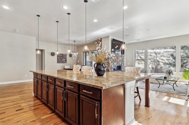 kitchen featuring decorative light fixtures, a stone fireplace, light wood-style flooring, and a kitchen breakfast bar